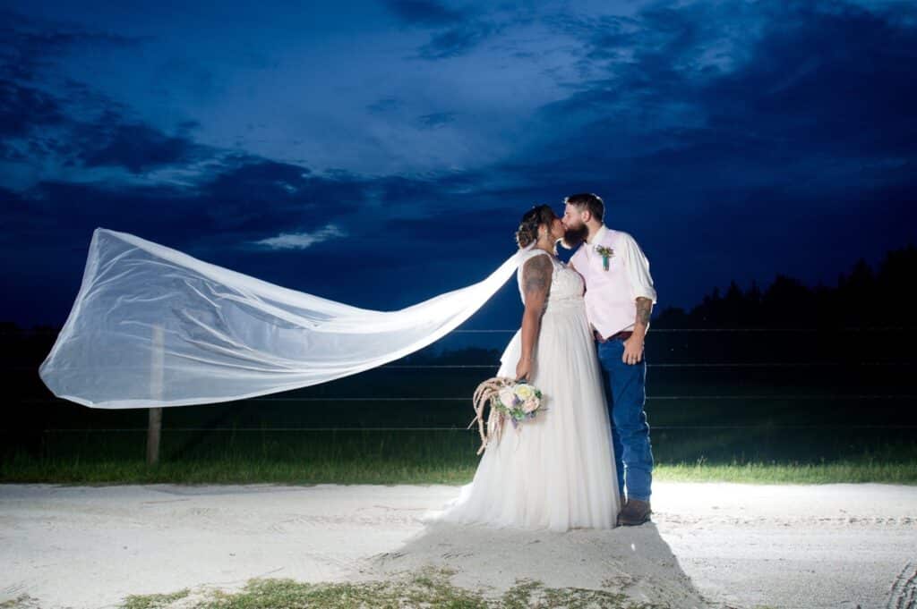 bride and groom kissing as bride's veil floats away at the Diamond L Venue in Volusia County, near Deltona, FL