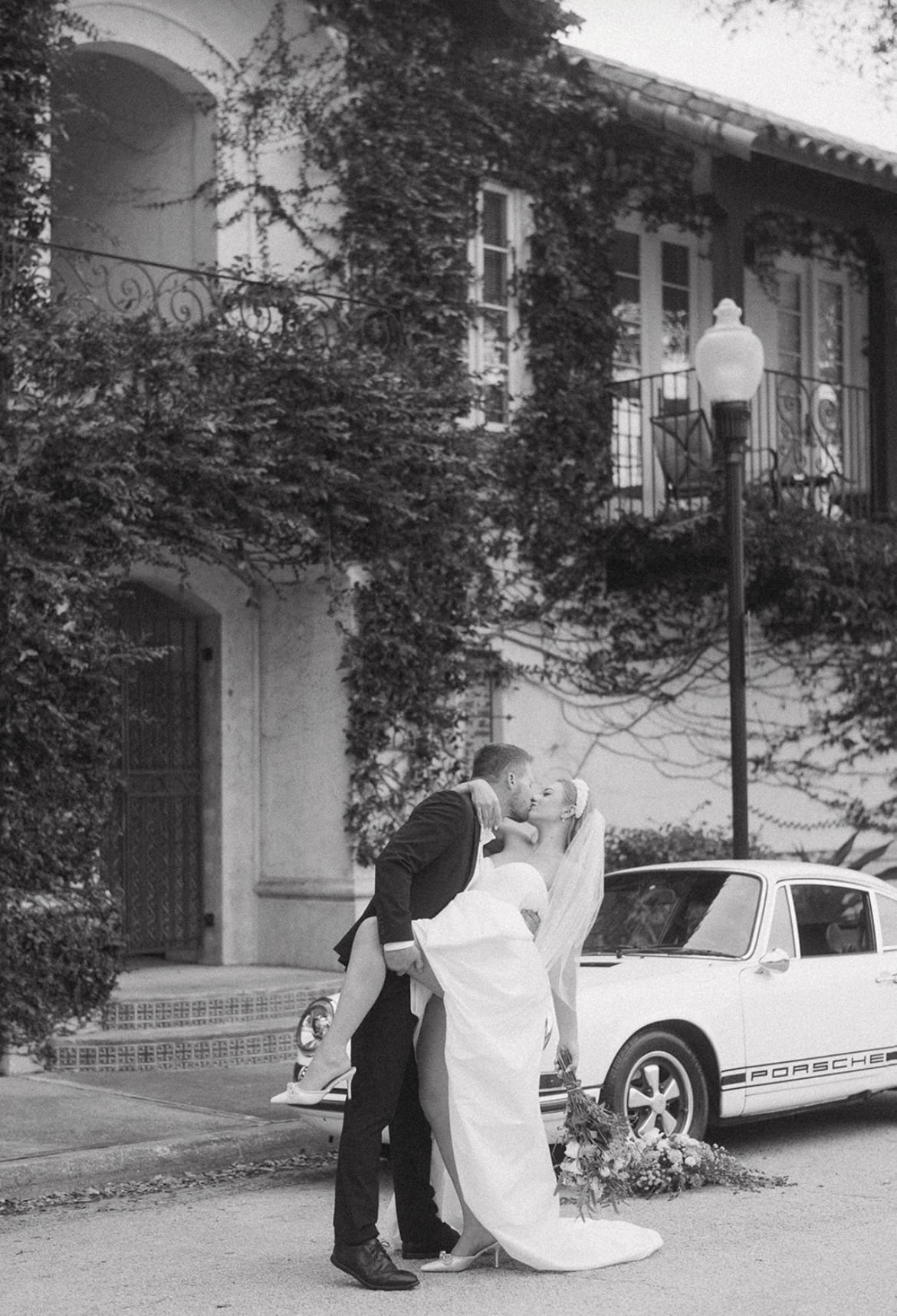 couple pose kissing in front of vintage white car for engagement picture