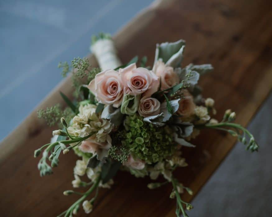 bouquet with handle wrapped in white ribbon with pink and white roses scattered in greenery