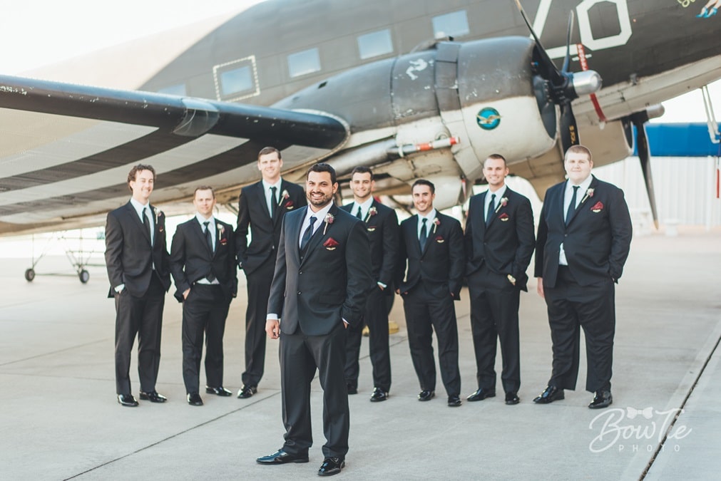 groom and groomsmen standing in front of vintage airplane at The Warbird Air Museum