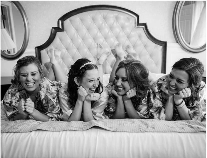 bride and bridesmaids smiling and laughing on bed getting ready for her wedding coordinated by Fairy Tales & Wedding Bells