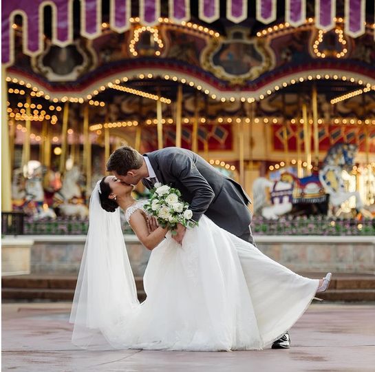 groom dips bride against a carousel backdrop at wedding coordinated by Fairy Tales & Wedding Bells