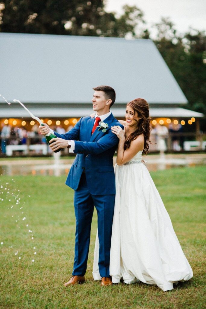 bride and groom popping champagne outside large wedding tent at October Oaks Farm