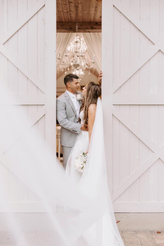 bride and groom laughing between white barn doors at October Oaks Farm