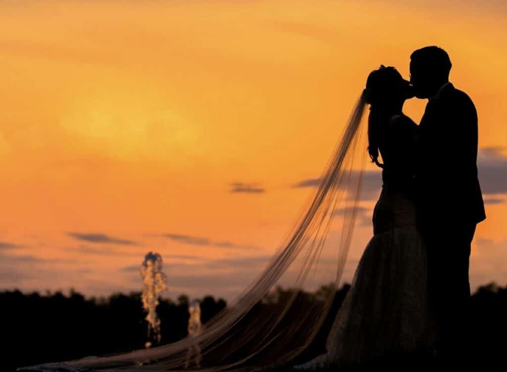 silhouette of bride and groom kissing against a burnt orange sky at October Oaks Farm