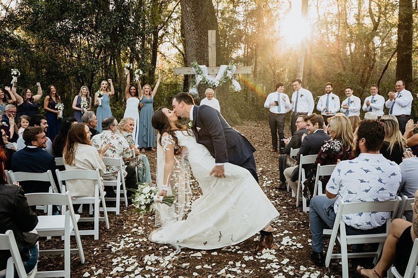 groom kissing his bride as sun peaks through the trees at October Oaks Farm