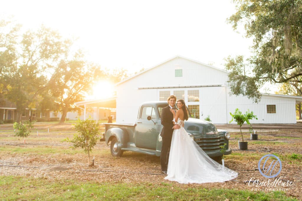 bride and groom in front of farmhouse and vintage pickup at Ever After Farms Citrus Barn at sunset