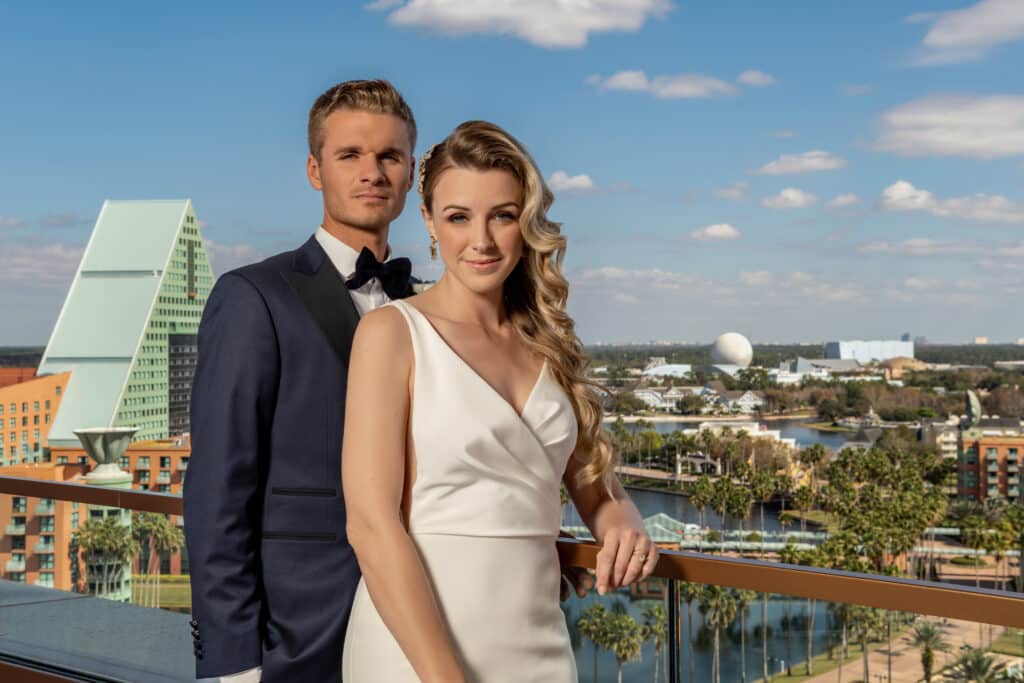 bride and groom standing on outdoor balcony at Walt Disney World Swan Reserve with Contemporary Hotel and resorts in the background at Walt Disney World