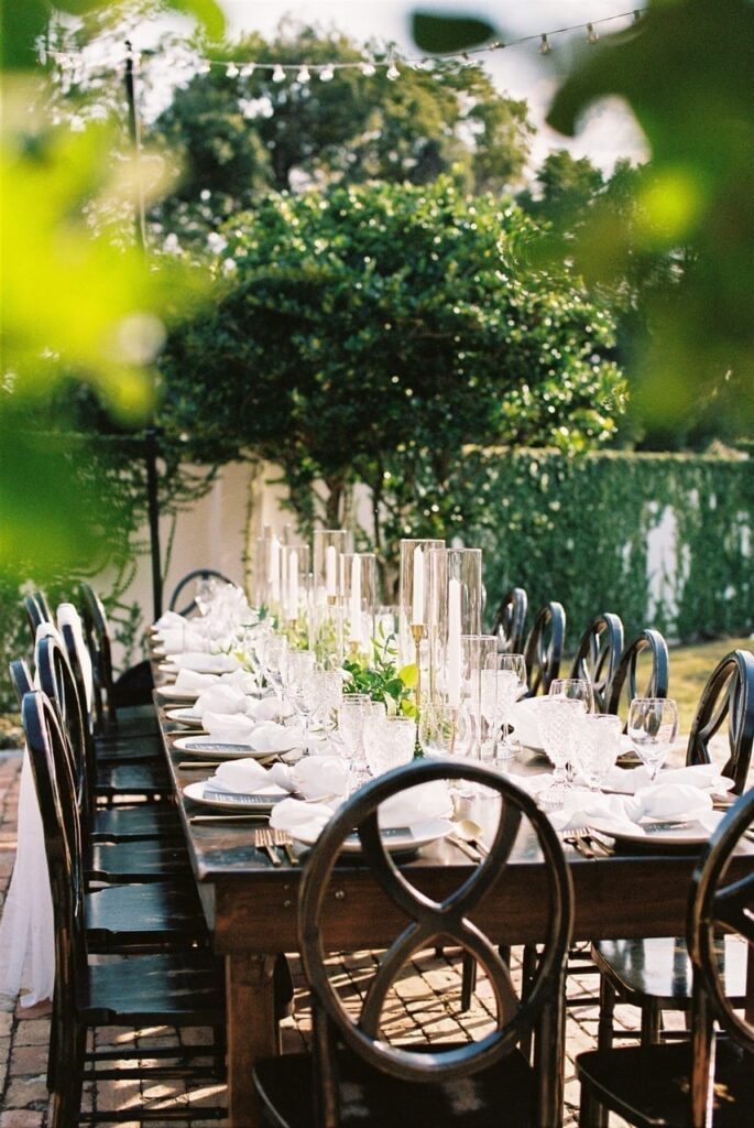 long wooden table set outdoors with white linens and tall centerpieces at the Chapel & Cellar