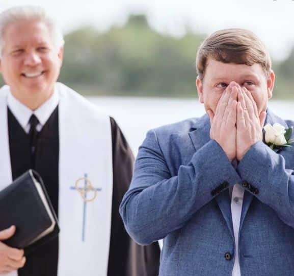 pastor looking on as groom covers his mouth in awe as he sees his bride at wedding coordinated by Fairy Tales & Wedding Bells