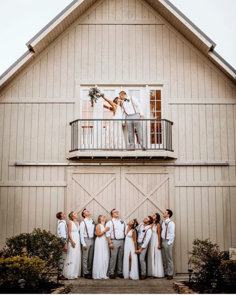 bride and groom kissing on balcony above bridal party at October Oaks Farm