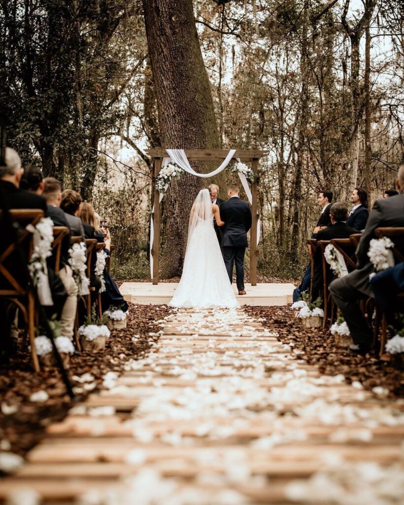 bride and groom at the end of long leaf strewn outdoor aisle at October Oaks Farm
