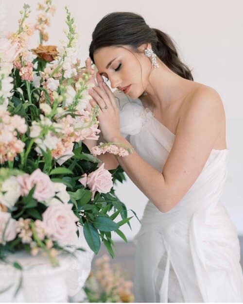 bride looking down at flowers and showing make-up done by Bronze + GLOW Beauty