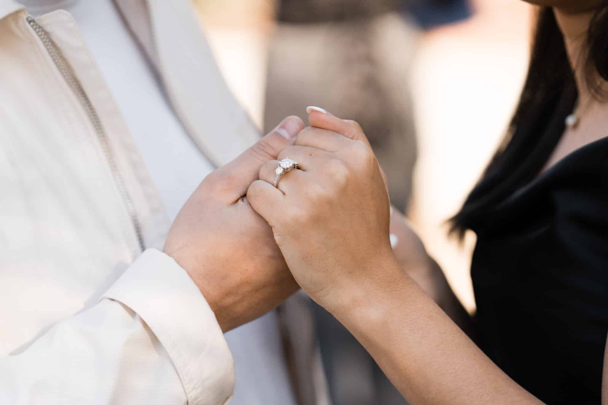 close up image of a couple holding hands and engagement ring predominantly showing