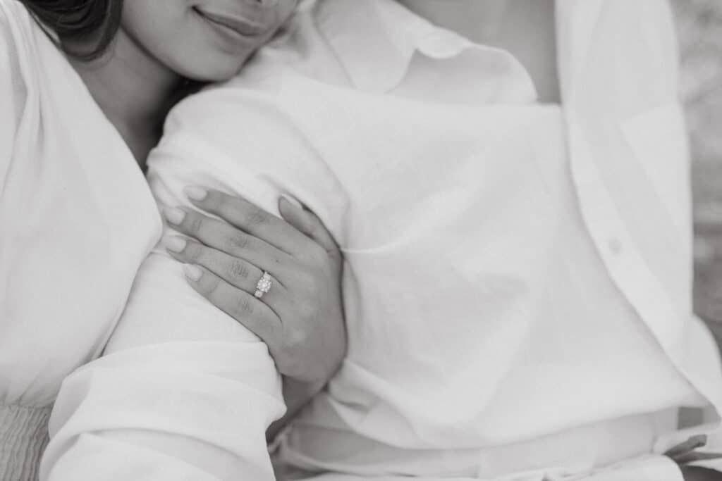 black and white image of woman holding man by the arm with engagement ring showing