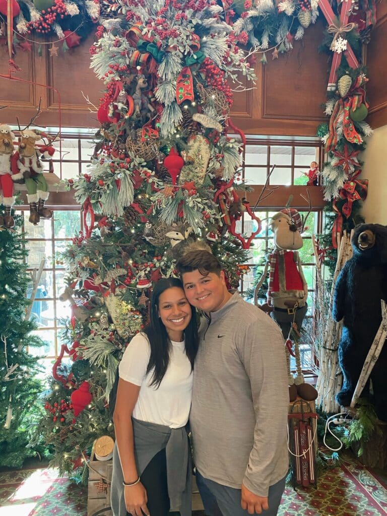 young man and woman stand together for picture in front of very decorated christmas tree