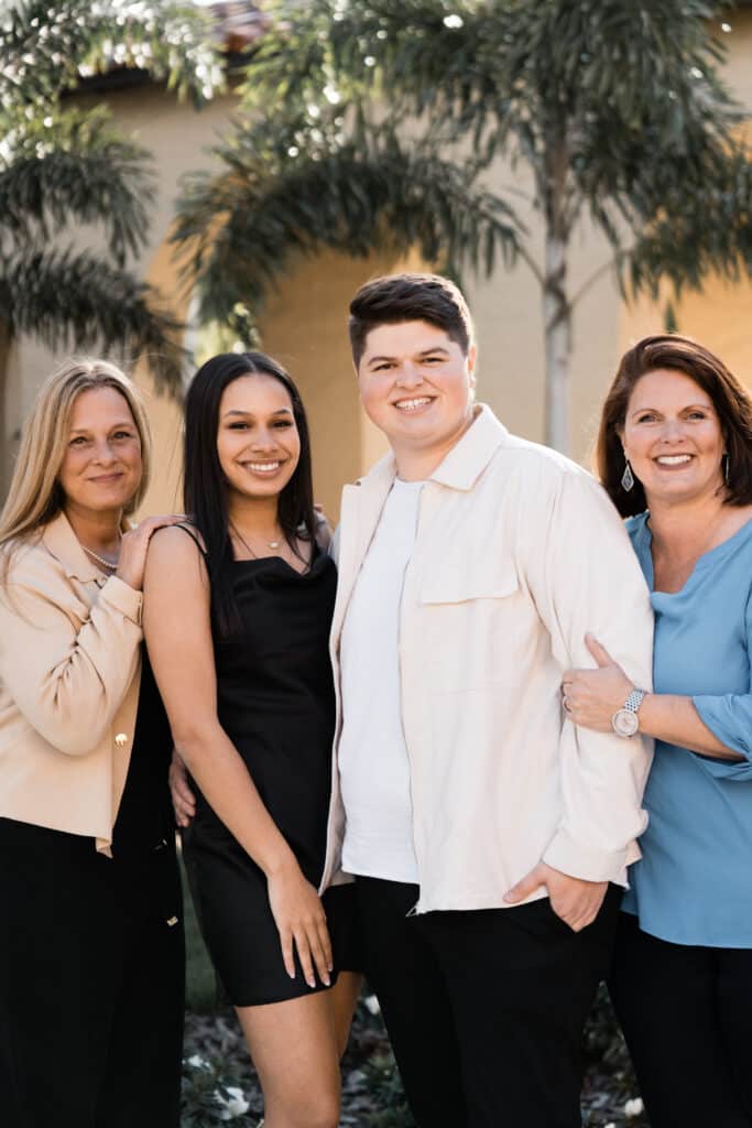 young couple stand together smiling with both of their mothers on either side of them smiling and hugging them