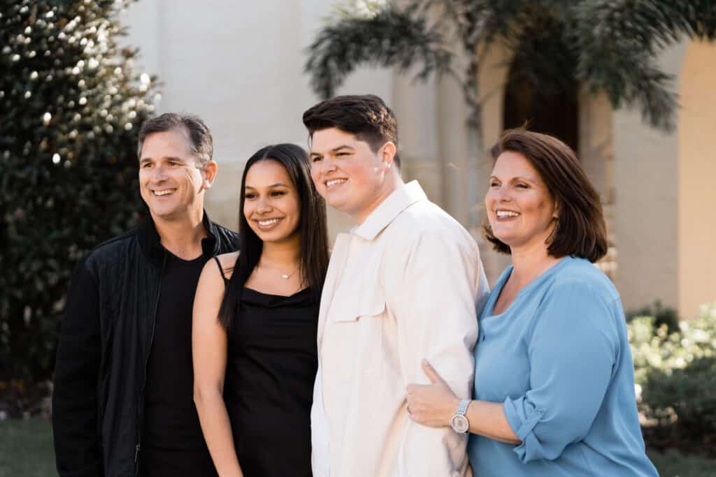young girl and man stand together smiling with an older man and woman on either side of them smiling at the camera