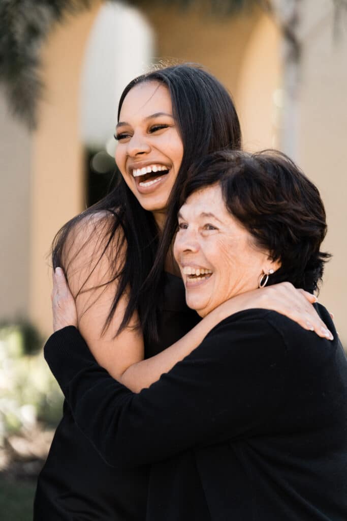 young woman hugs older woman tightly while smiling with mouth open