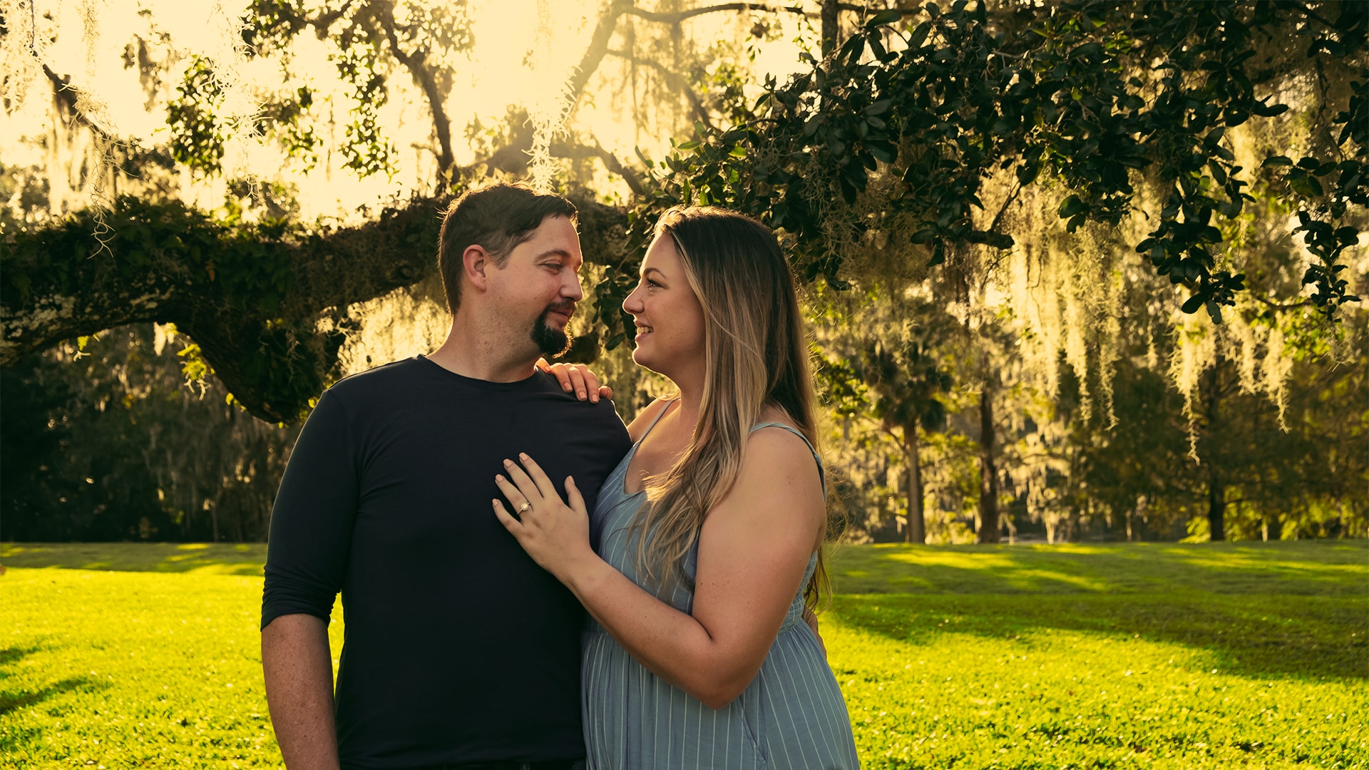 couple poses together in front of trees with moss hanging from them at surprise marriage proposal at leu gardens