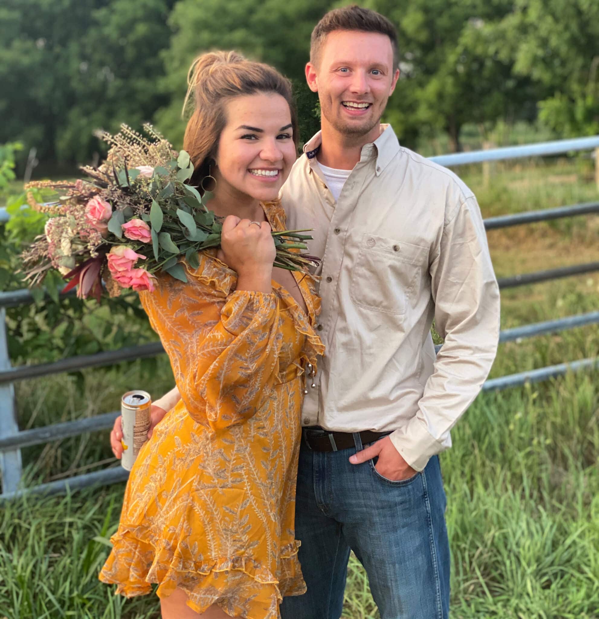 woman in bright yellow dress smiles holding bouquet of wild flowers with man in long sleeve button down shirt stands next to her smiling