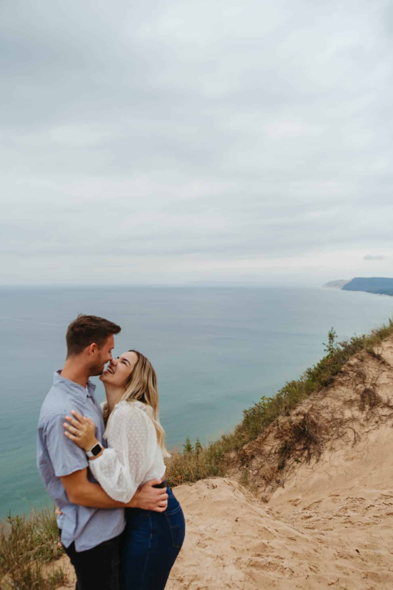 couple kissing outside on elevated land overlooking a body of bright blue water