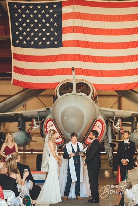 bride and groom saying their vows in front of vintage airplane and American flag in an airplane hangar at The Warbird Air Museum