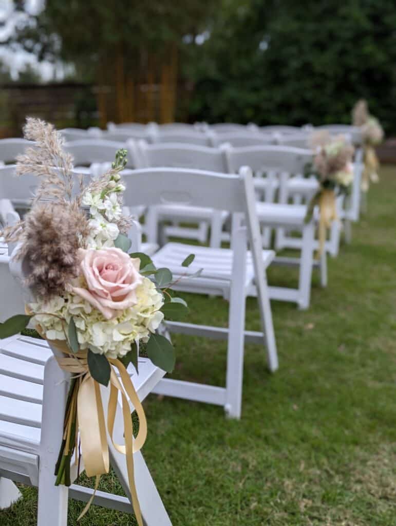 White chairs, waiting for ceremony guess with sprays of pink flowers and ribbons coordinated by Events by Rachel