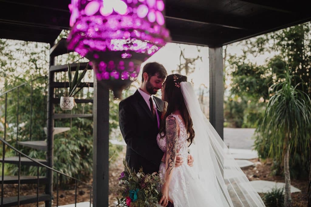 bride and groom under outside patio with circular stairs and purple chandelier at Wanderlust Okto