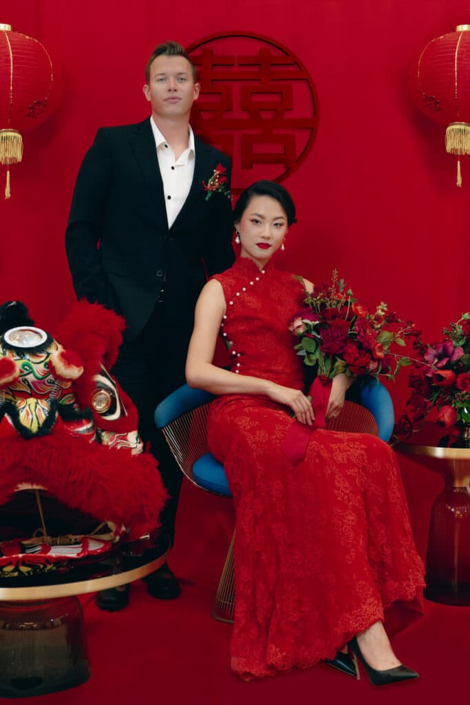 photo by Bouquet Photography of formal photo of couple posing for wedding photo with woman in red dress and Chinese symbols on the wall