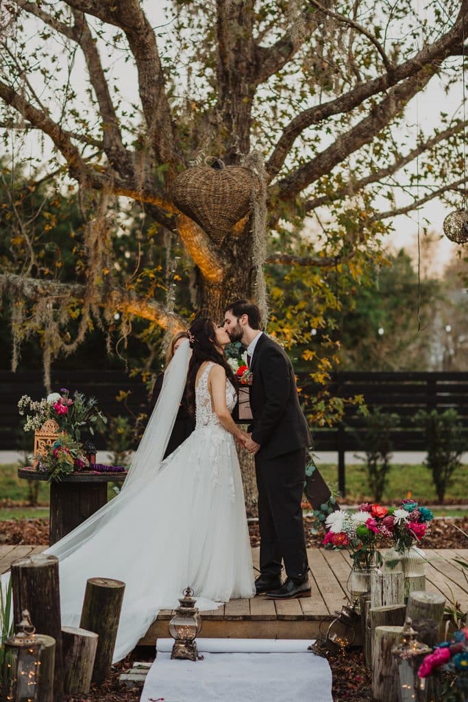 bride and groom kissing on wooden dais under oak tree at Wanderlust Okto