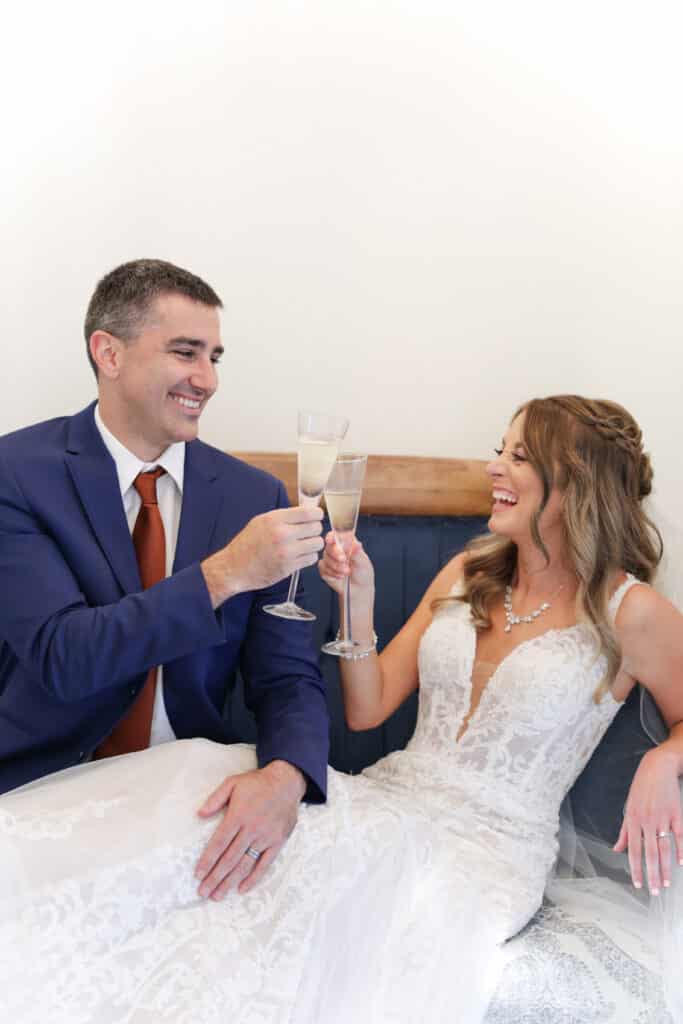 photo of bride and groom sitting on a blue couch toasting each other with champagne by Sylvia Santos Photography