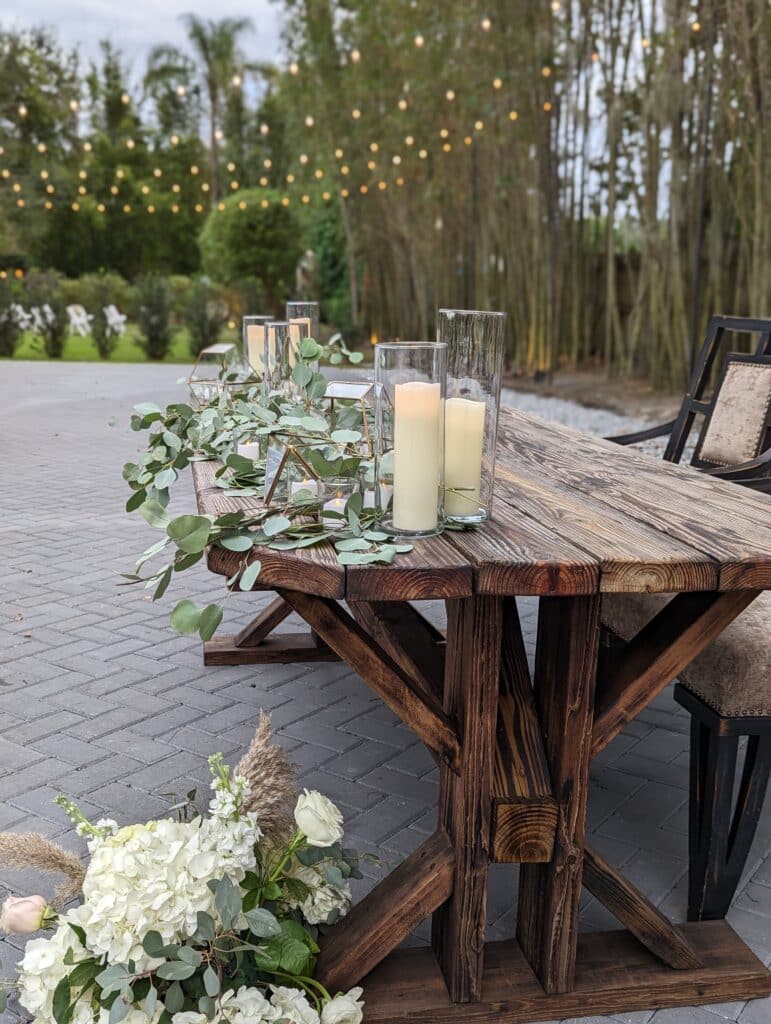 Wooden trellis table with candles and flowers outdoors under market lights coordinated by Events by Rachel