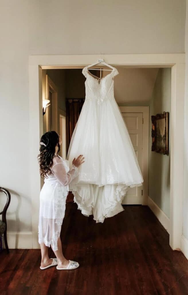 bride looking at hanging wedding dress waiting to be put on at THE 1883 Historic Venue