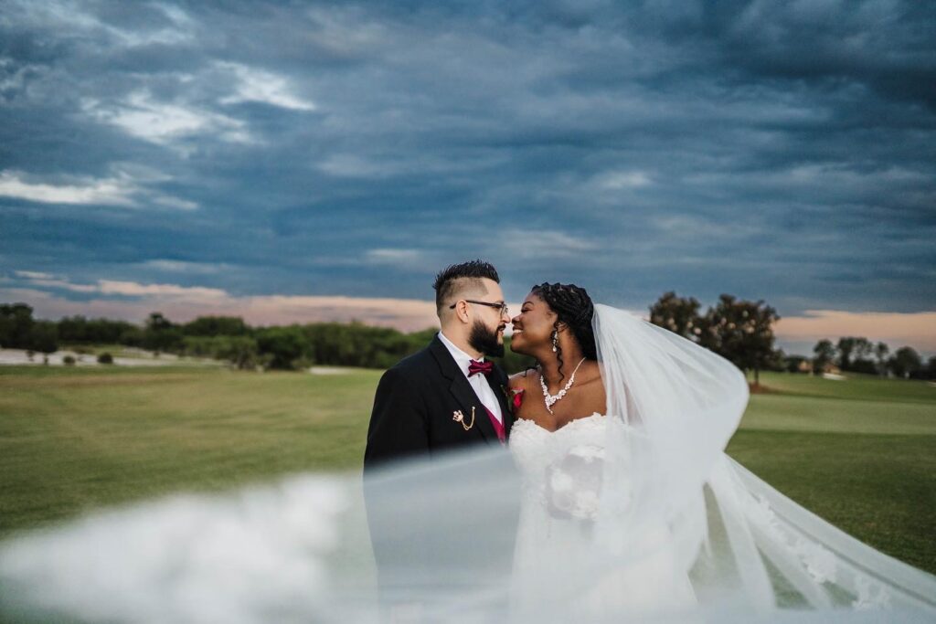 photo by Taylor Kuperberg Photography of bride and groom kissing under a big blue sky and her floating veil