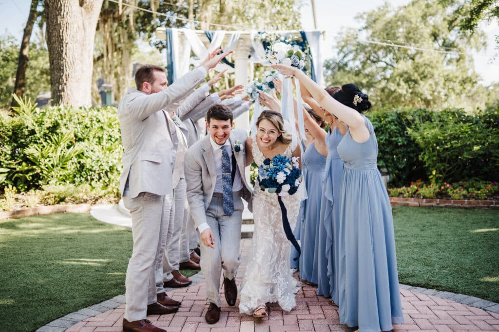 photo by Taylor Kuperberg Photography of bride and groom walking under arch of bridal party with shades of blue in flower arrangements and bridesmaids dresses