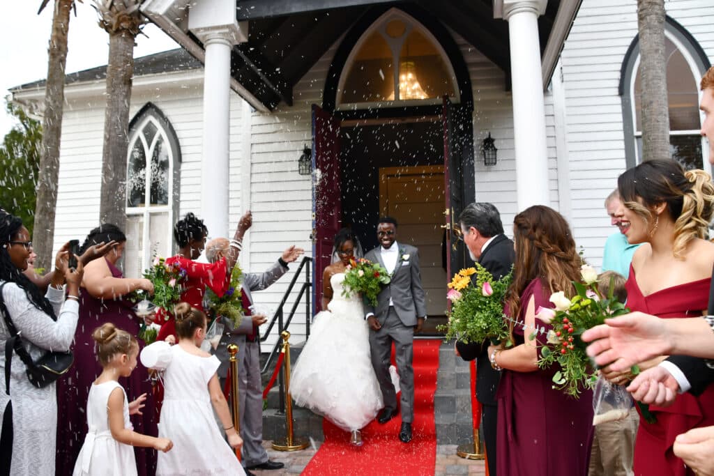 bride and groom leaving THE 1883 Historic Venue on a red carpet as guests wave and shout to them