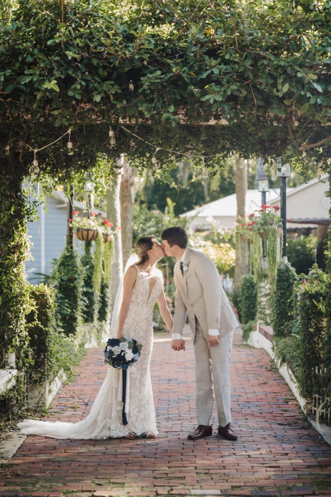 photo by Taylor Kuperberg Photography of bride and groom kissing on a brick walkway covered by green tree canopy