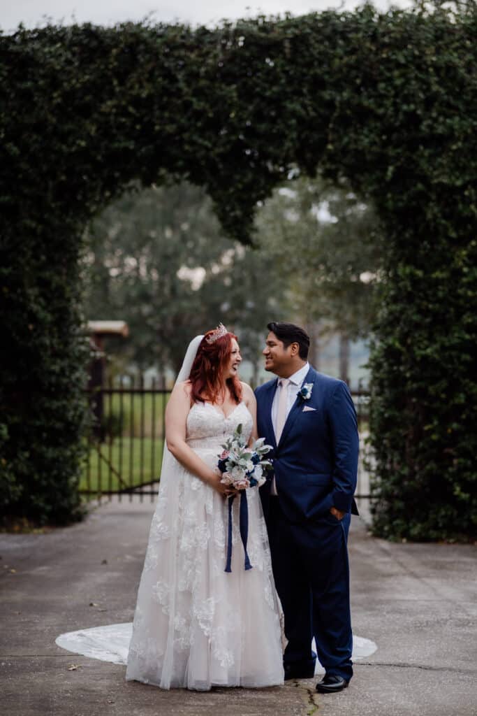 photo by Taylor Kuperberg Photography of bride and groom standing in a courtyard with a heart shaped greenery wall behind them