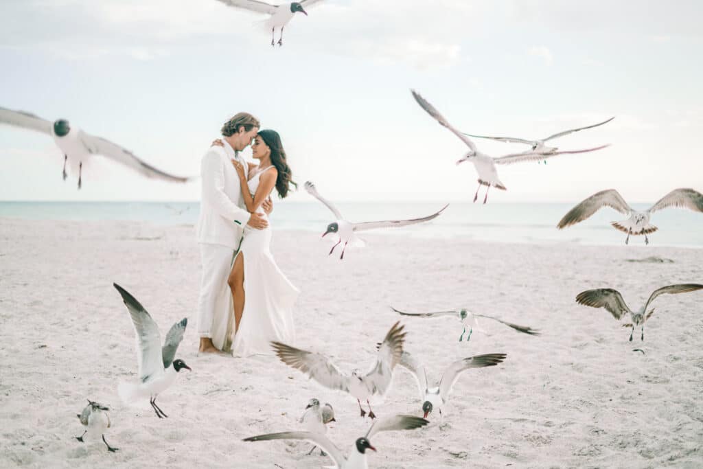 photo by Bouquet Photography of bride and groom on the beach surrounded by seagulls in the air