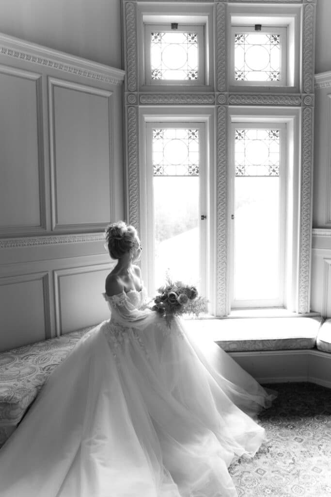 black and white photo of bride with tulle skirt looking out windows by Sylvia Santos Photography