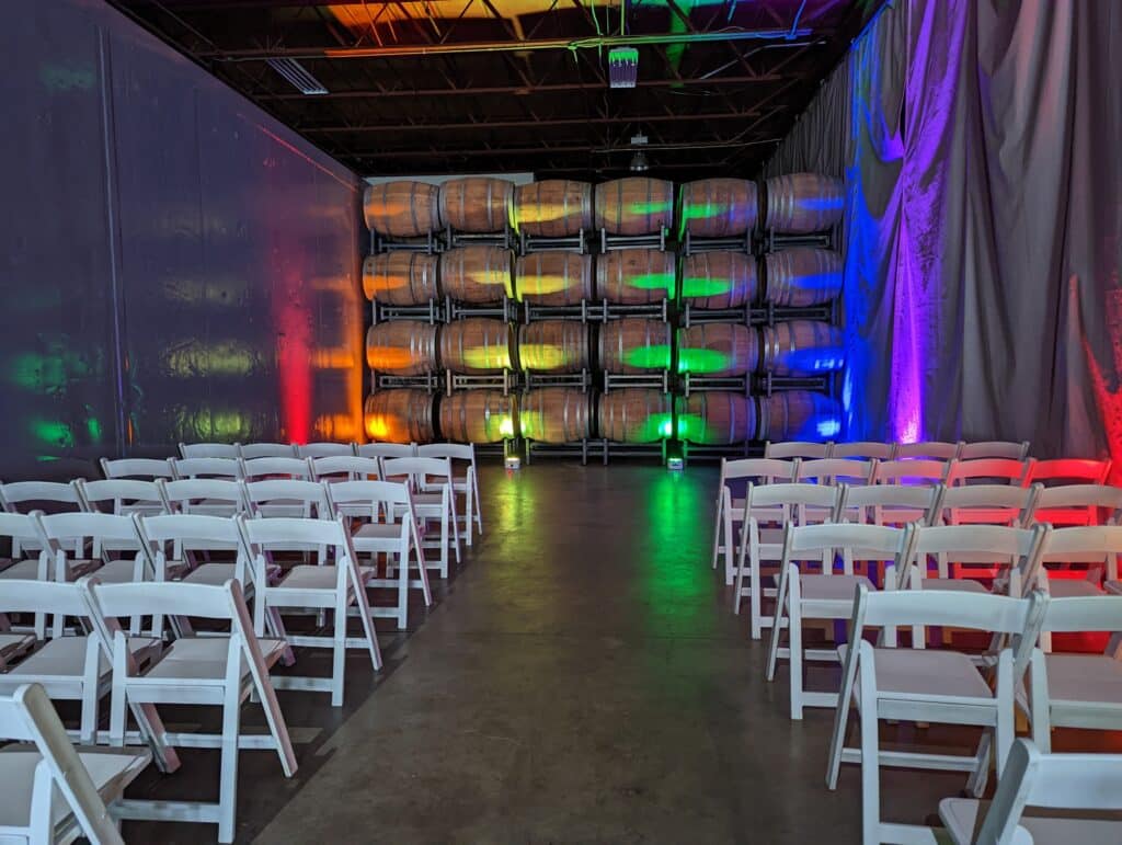Rainbow of up lights at indoor ceremony with white chairs coordinated by Events by Rachel