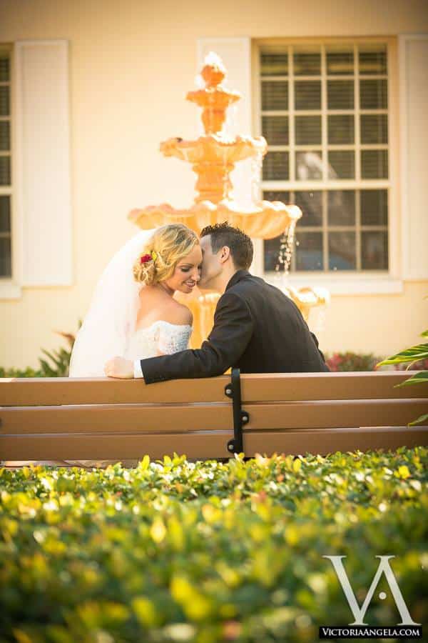 groom whispering to his bride as they sit on a bench beside an outdoor fountain at The University Club of Winter Park