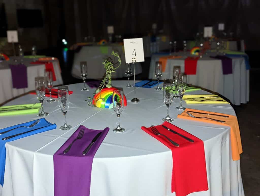 Colorful, rainbow centerpiece, and napkins draped on white tablecloth coordinated by Events by Rachel