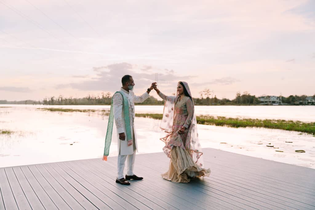 bride in a sari and groom in traditional garments dancing on a wooden dock at sunset photo by Bouquet Photography