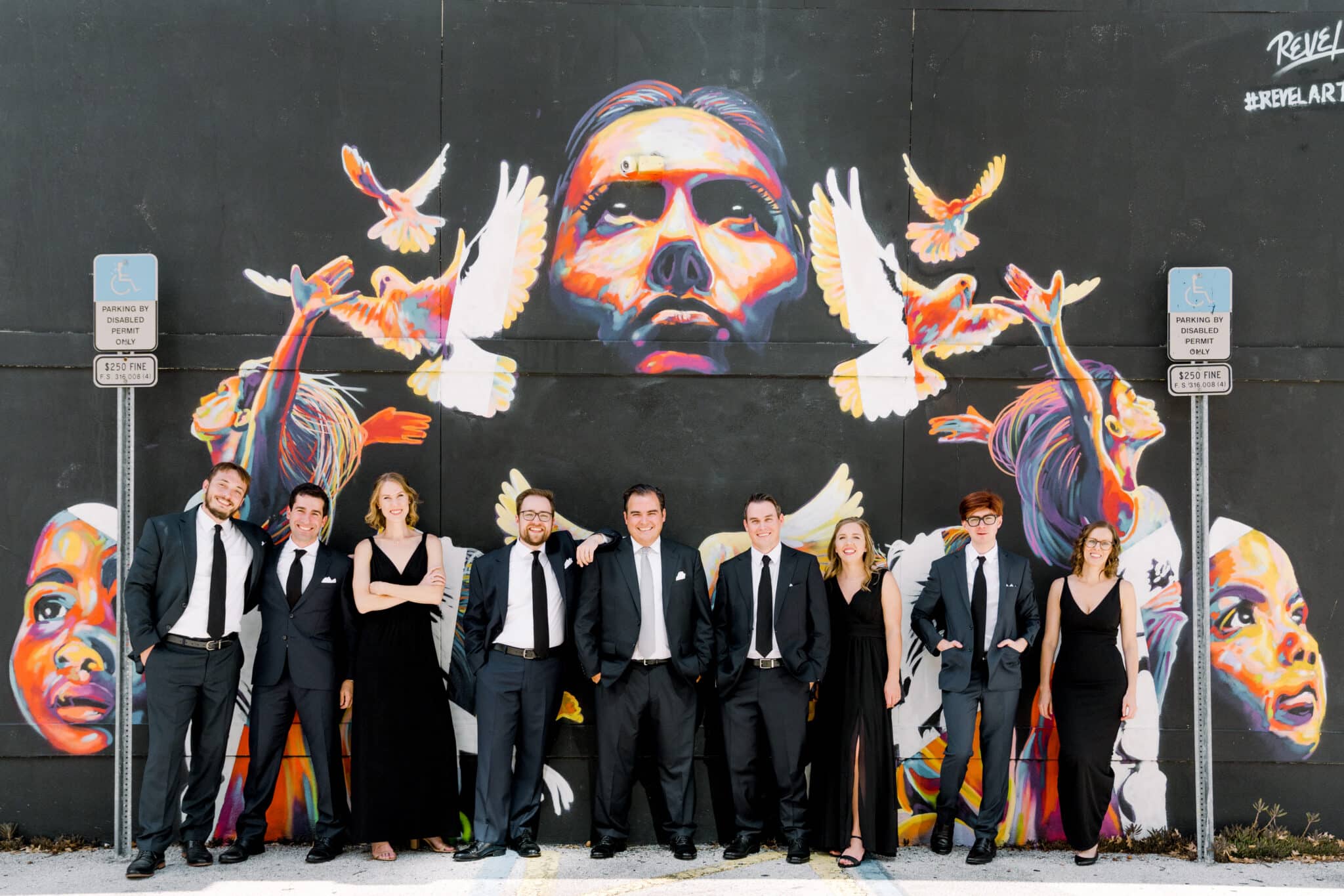 Florida groom stands with his mixed gender wedding party against wall art mural