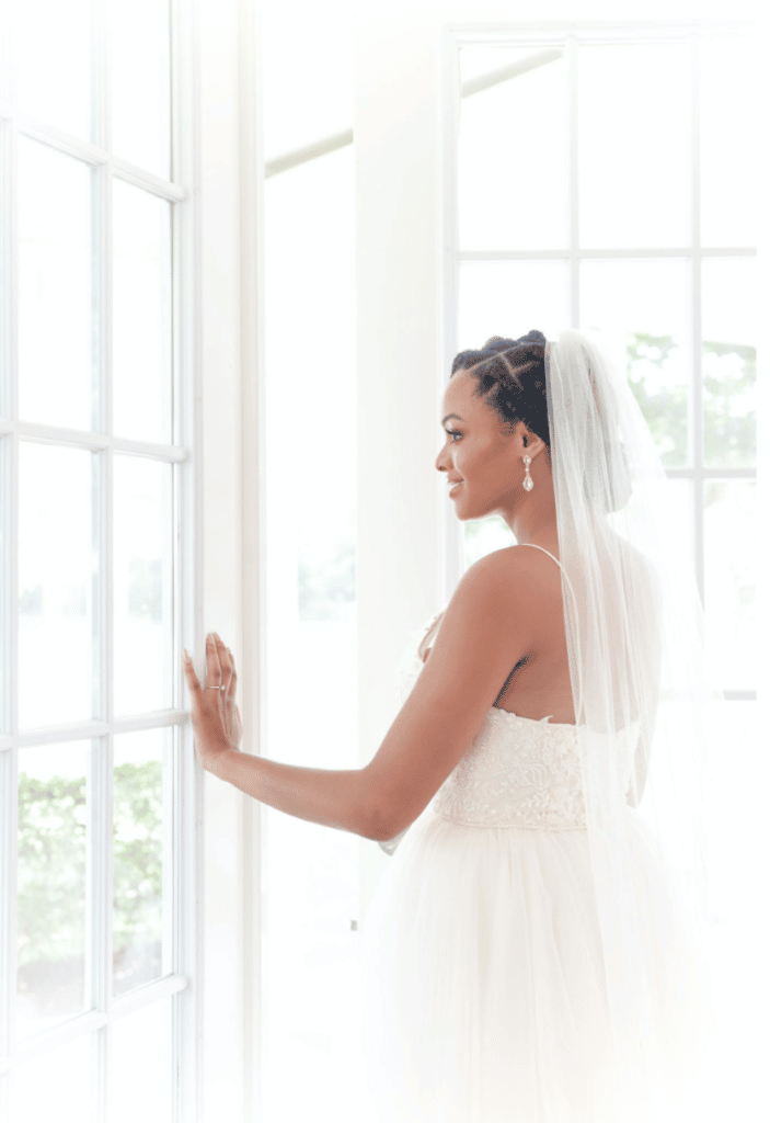 photo of bride standing next to large paned windows and looking out of them by Sylvia Santos Photography