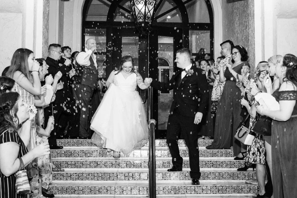 black and white photo of bride and groom leaving wedding reception as friends and family throw confetti at La Cita Country Club