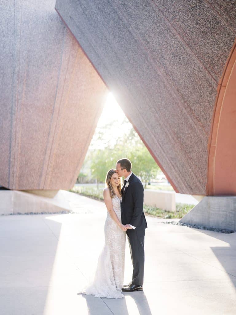 bride and groom under modern arch of buildings with sun setting at the Winter Park Events Center