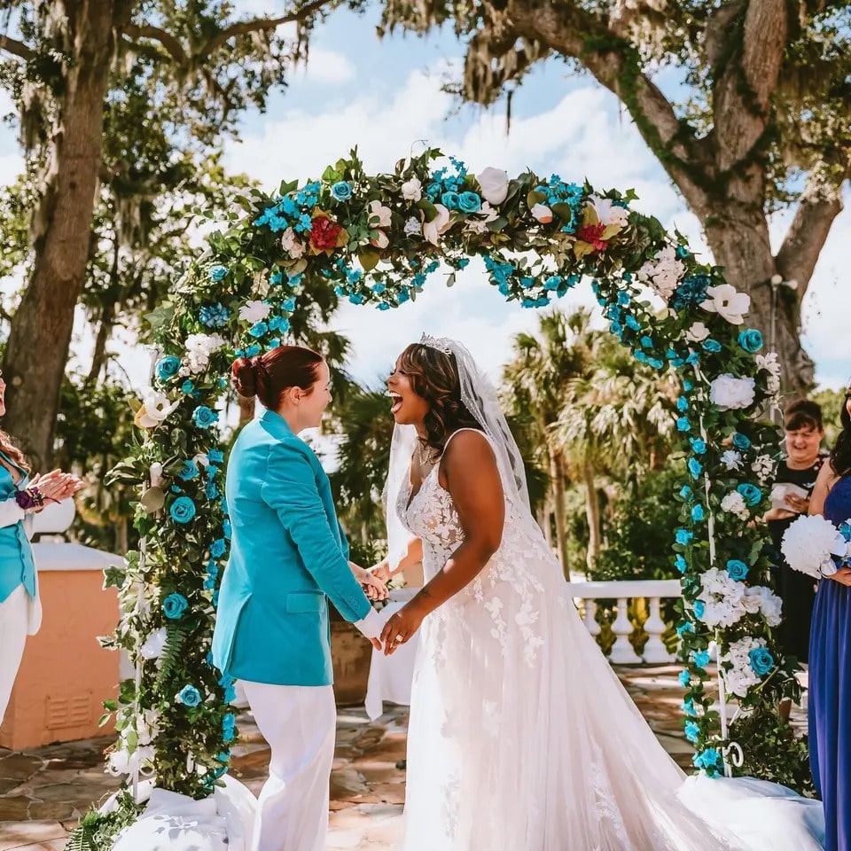 wedding couple under arch of turquoise, white and red flowers at La Cita Country Club
